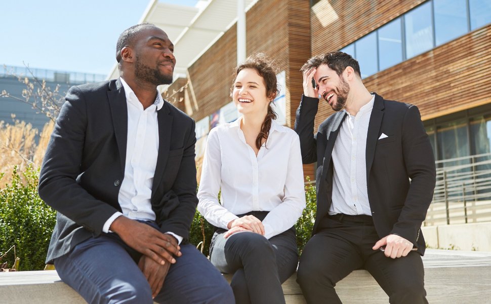 Drei junge Kollegen sitzen zusammen vor einem Gebäude und unterhalten sich erfreut.