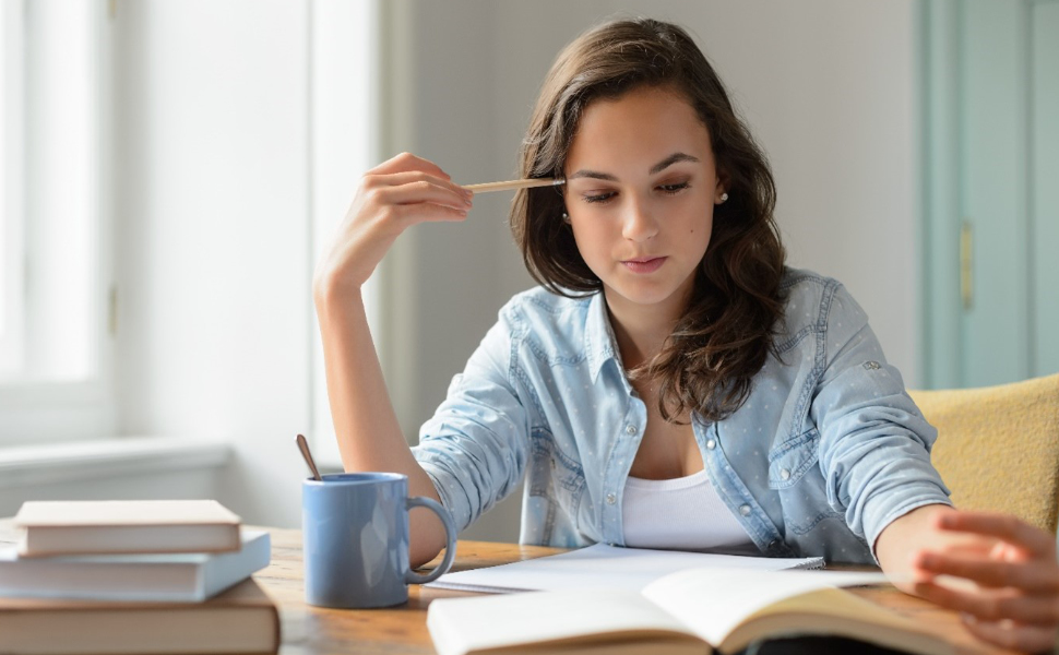 Frau sitzt lernend am Schreibtisch vor einem aufgeschlagenen Buch