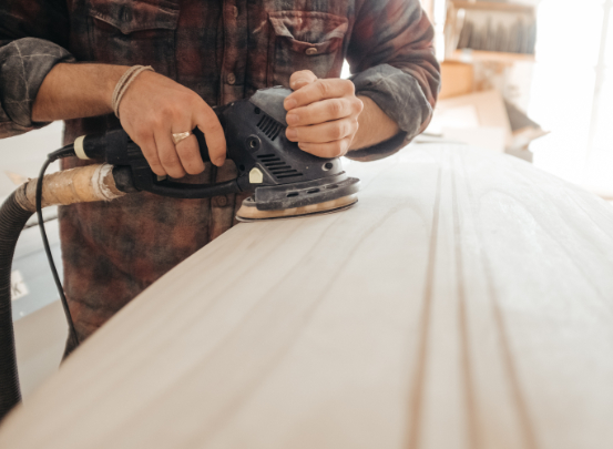 Ein Tischler schleift eine Holzplatte ab.