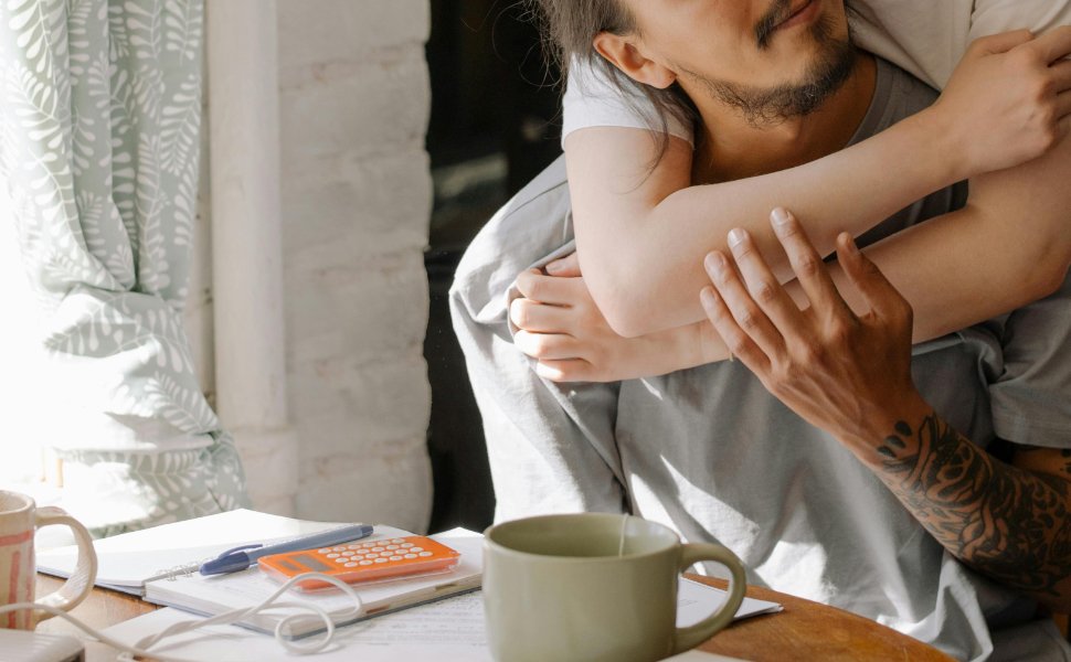 Mann sitzt am Schreibtisch und wird von Frau umarmt