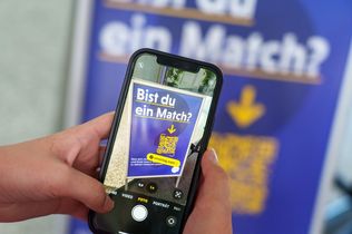 Ein Smartphone wird vor ein Plakat mit QR-Code gehalten