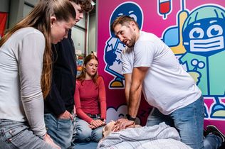 Ein Mann zeigt Jugendlichen an einer Übungspuppe, wie eine Reanimation abläuft.