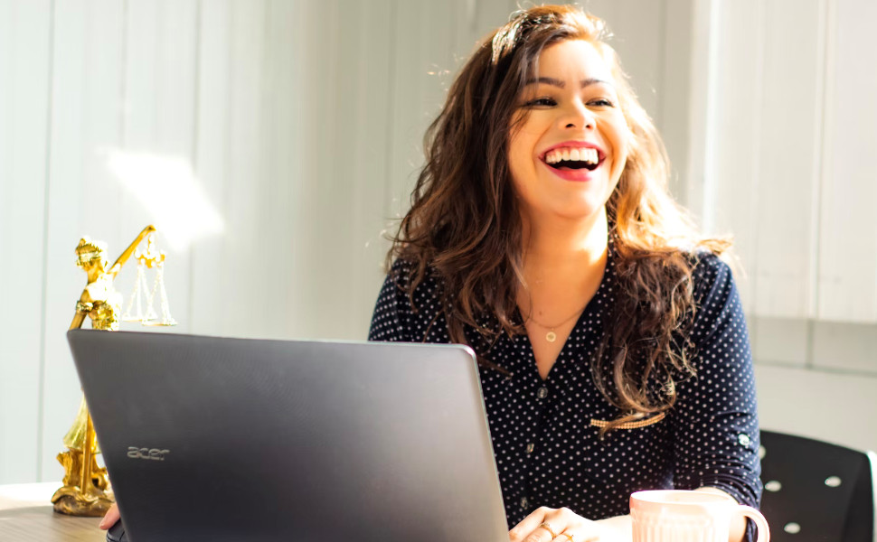 Frau lacht bei der Arbeit vor ihrem Notebook.