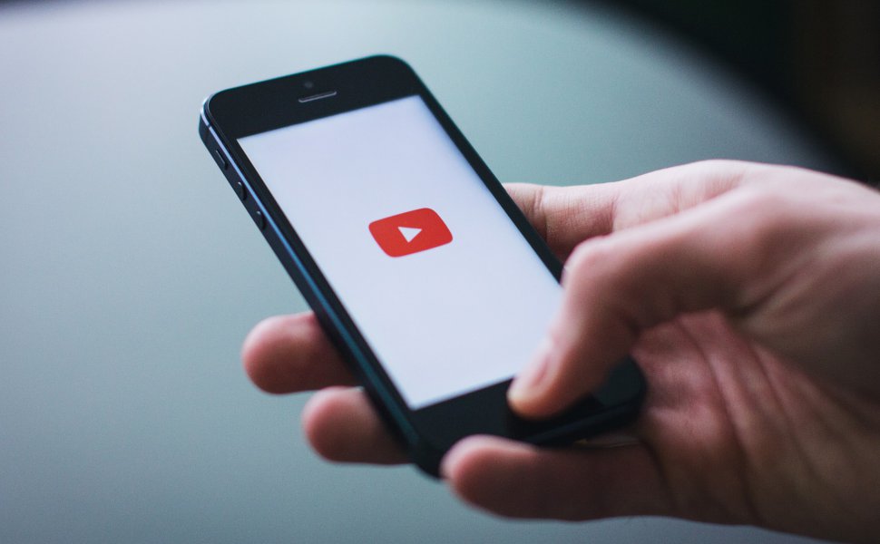 Hand, die Smartphone hält. Auf Smartphone erscheint Youtube-Logo.