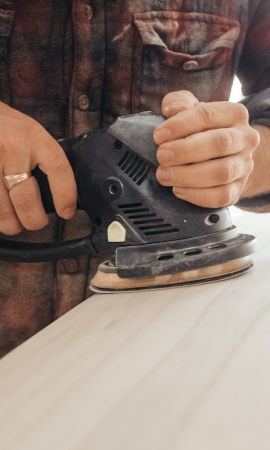 Der Tischler schleift eine Holzplatte ab.